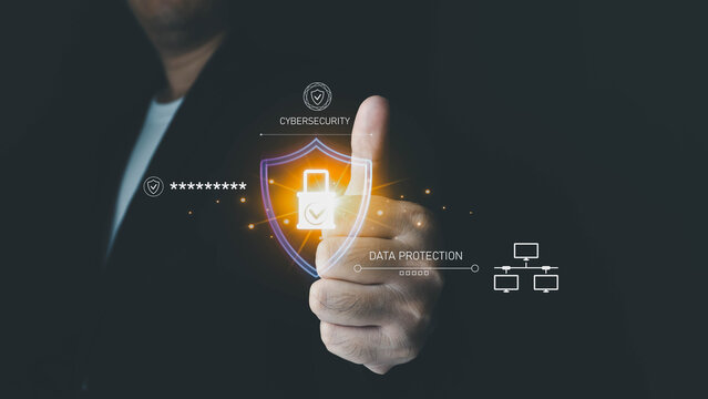 A businessman uses his thumb to touch a holographic shield icon, illustrating the concept of cybersecurity and data protection on a digital interface.