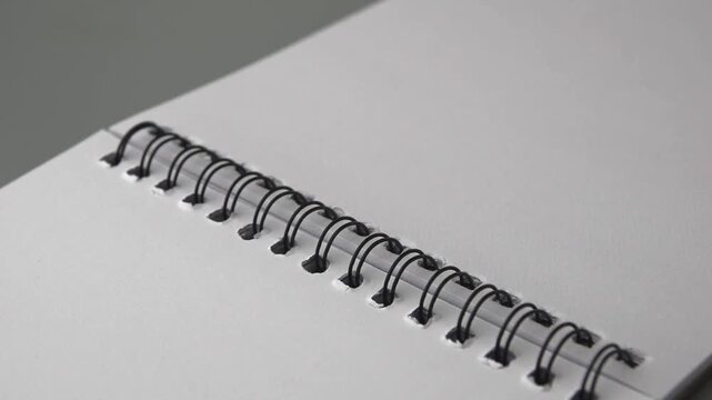 close-up of open spiral notebook with black wire binding and blank white pages, ready for notes, drawing or planning, symbolizing new ideas and creativity, soft focus and slow motion in 60fps