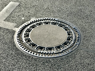 Iron hatch with a pattern above an observation well is located on auto road in daytime