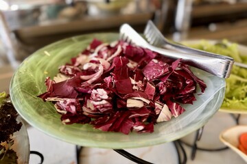 Fresh salad with tongs, a mix of leaf vegetables and ingredients on a plate