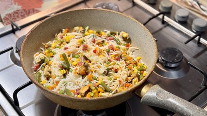 Cellophane noodles, mussels, corn, carrots, bean pods preparing in frying pan on the gas stove