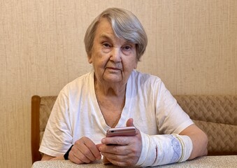 Portrait an elderly woman with broken arm width cast for the arm sitting at couch holding...