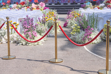 Gold pole and red velvet rope entrance barrier on chairs in row decorative with colorful multicolored flower for outdoor event background