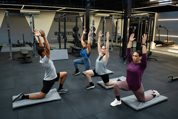 Group of latin fitness enthusiasts performing a low lunge stretch, demonstrating flexibility and strength during a fitness class in a contemporary gym