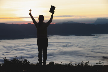 Woman praying with the bible on the mountain at sunrise in the morning.