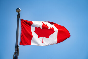 View of Canadian flag waving in clear blue sky.
