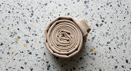 Rolled beige sweatshirt on a terrazzo surface creating a circular pattern and minimalist fashion aesthetic for apparel ads