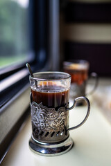 Close up tea in glass with metal holder and spoon on train table near window. Travel drink, railway tea, onboard beverage, warm drink journey, classic train service, retro long distance comfort