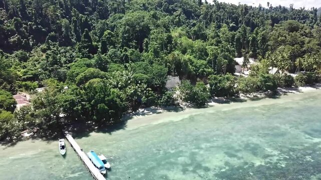 Beautiful 4K aerial footage of a wooden pier with boats anchored in clear turquoise shallow water, surrounded by lush tropical forest coastline.