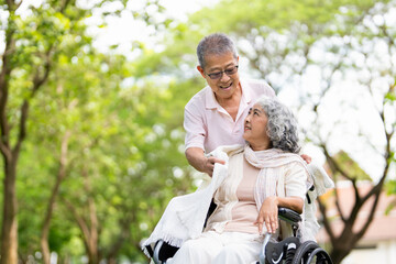 Senior woman in wheelchair walking with old man in park. Elderly family couple. man supporting taking care of paralyzed woman in chair for people with disability outdoor. Rehabilitation.