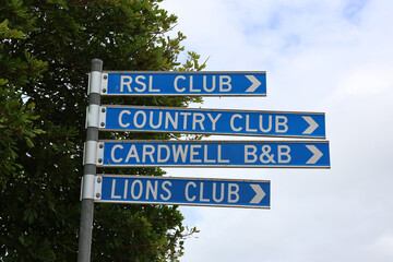 Blue signs mounted on a metal pole pointing towards the RSL Club, Country Club, Cardwell B&B and Lions Club in Cardwell, Queensland, Australia