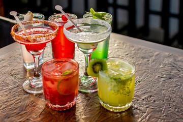 Vibrant assortment of colorful cocktails on a rustic wooden bar table, perfect for a happy hour party or summer celebration menu.