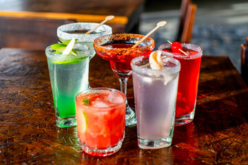 Vibrant assortment of colorful cocktails on a rustic wooden bar table, perfect for a happy hour party or summer celebration menu.