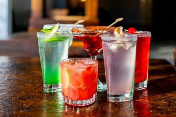 Vibrant assortment of colorful cocktails on a rustic wooden bar table, perfect for a happy hour party or summer celebration menu.