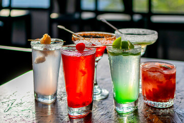 Vibrant assortment of colorful cocktails on a rustic wooden bar table, perfect for a happy hour party or summer celebration menu.