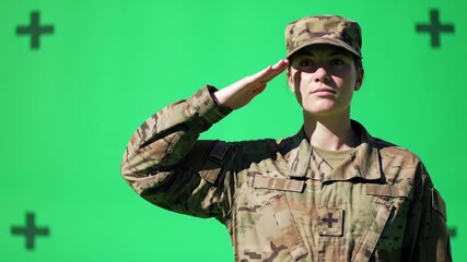 A female soldier in camouflage uniform salutes against a bright green screen backdrop.