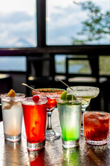 Vibrant assortment of colorful cocktails on a rustic wooden bar table, perfect for a happy hour party or summer celebration menu.