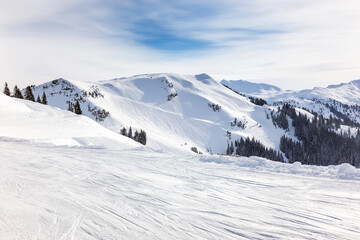 Winter mountain scene with snowy slopes, ski tracks visible, bright cold sky, seasonal holiday background.

