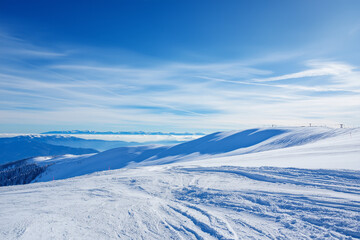 Winter mountain scene with snowy slopes, ski tracks visible, bright cold sky, seasonal holiday background.

