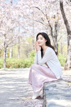 Young Asian female sitting on park bench surrounded by cherry blossoms in spring
