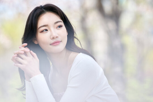 Young Asian female sitting on park bench surrounded by cherry blossoms in spring