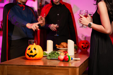 Friends celebrate a lively Halloween party with costumes, pumpkin lanterns, wine, delicious food on the table. The night is filled with laughter, colorful lights, and festive energy for seasonal joy.