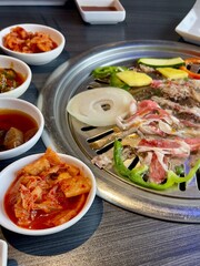Korean BBQ on a round grill with kimchi, onion and vegetables. Wide composition with copy space.