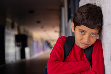 Fototapeta premium School hallway, young boy in red shirt leaning against wall, looking thoughtful, copy space