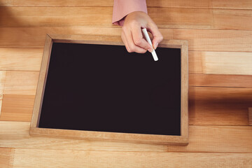 Hand holding chalk writing on small blackboard on wooden desk, copy space