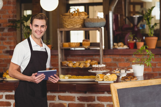 Barista holding tablet smiling in bakery with fresh pastries and bread