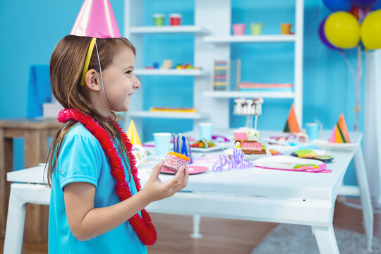 Girl celebrating birthday party indoors, holding cupcake and smiling joyfully - Powered by Adobe