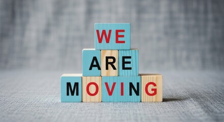 Stacked blocks spell "We Are Moving" on textured gray fabric background