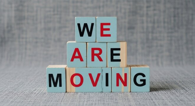 Stacked wooden blocks spell "WE ARE MOVING" on a textured gray background