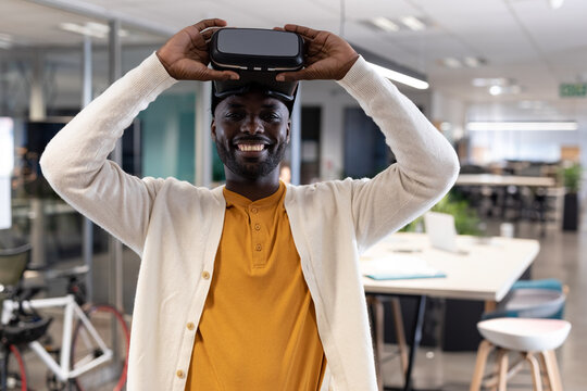 African American young adult smiling while holding virtual reality headset at modern office