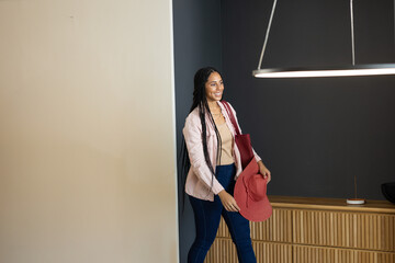 Mid adult multiracial woman holding red floppy hat and matching tote bag in modern lounge