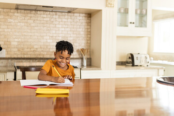 African American child girl writing in notebook in home kitchen at table with pencil, copy space