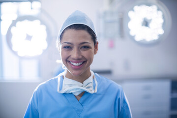 Female surgeon standing in bright surgical suite under overhead lights wearing blue scrubs and mask