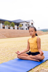 Girl meditating on yoga mat outside school, practicing mindfulness and relaxation, copy space