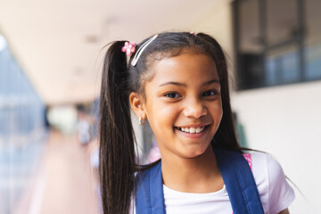 Smiling girl with backpack standing in school hallway, feeling happy and confident