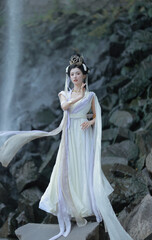 Fototapeta premium Elegant woman in a flowing silk dress standing by a waterfall.