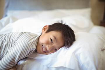 Asian boy lying in bedroom wearing striped pajama top, smiling and resting head on white pillow