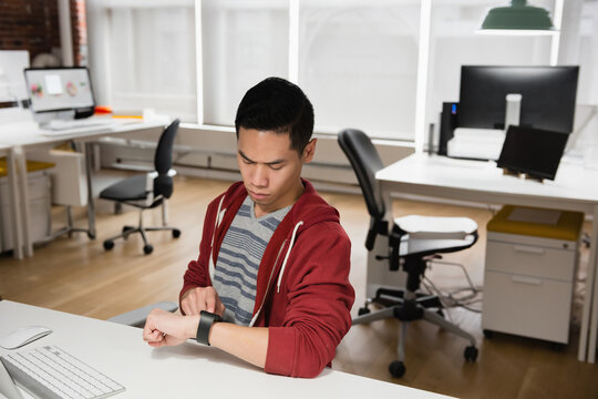 Young man checking smartwatch in modern office, concentrating on task