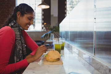 Smiling woman enjoying sandwich and green juice at cozy cafe counter, copy space