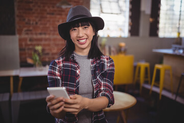 Smiling woman in hat using smartphone in trendy urban cafe