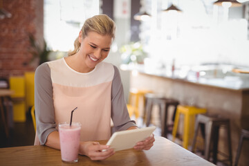 Smiling woman using tablet while enjoying smoothie in cozy cafe, copy space