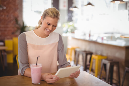 Smiling woman using tablet while enjoying smoothie in cozy cafe, copy space