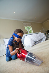 Red vacuum cleaner moving across beige carpet by bed with white linens and gray throw