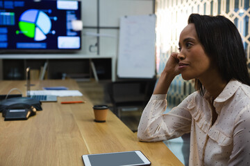 Businesswoman contemplating at conference table with tablet and coffee cup nearby, copy space