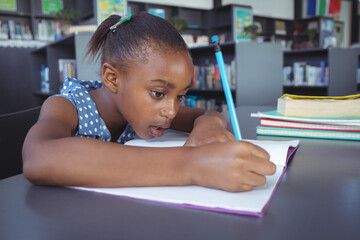 In school, focused girl writing in notebook at library table, concentrating hard