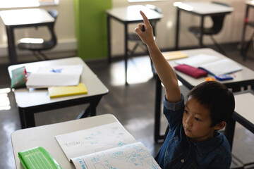 In school, young boy raising hand in classroom, eager to answer question, copy space